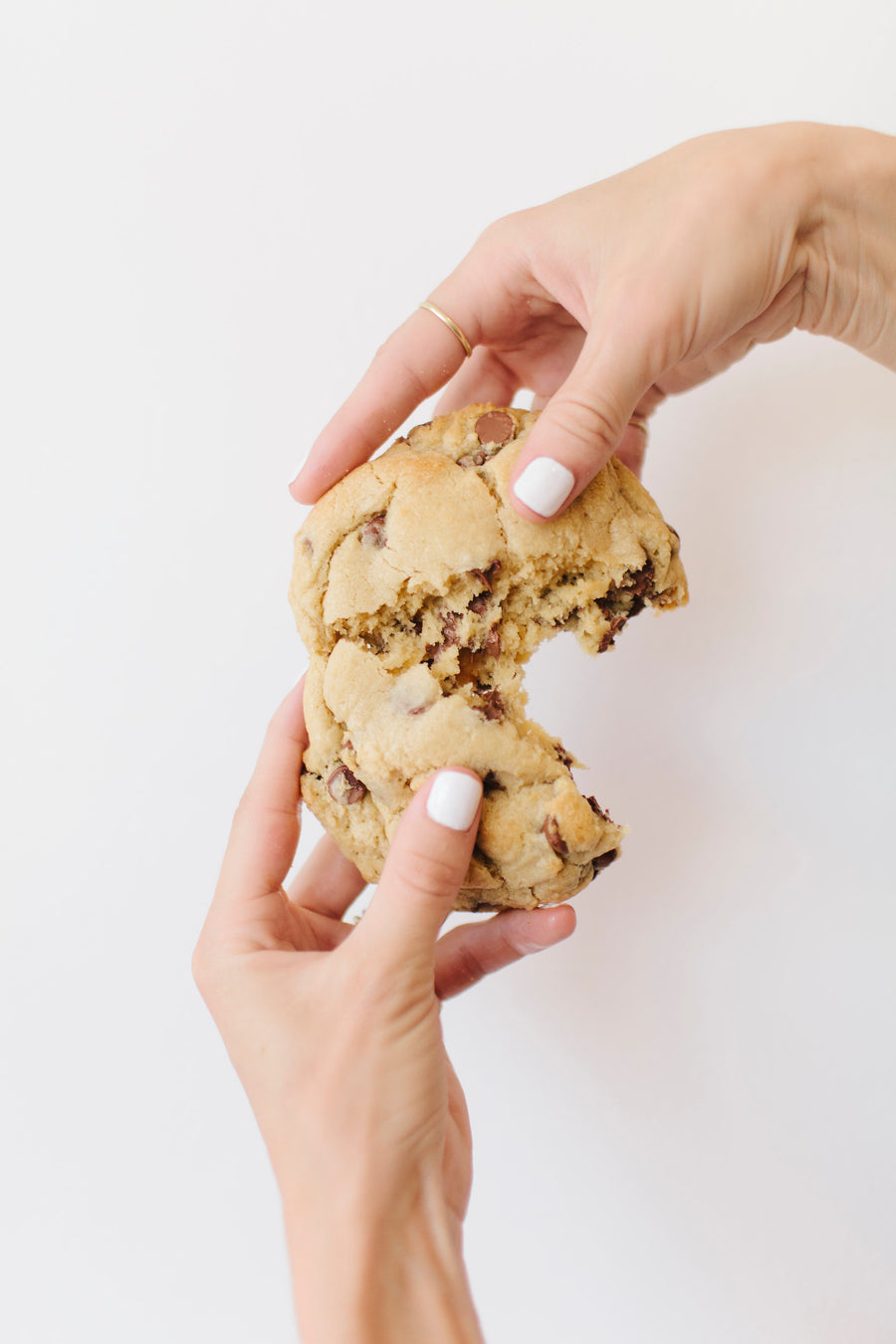 A warm, gooey Chip cookie held in hand with a bite taken out